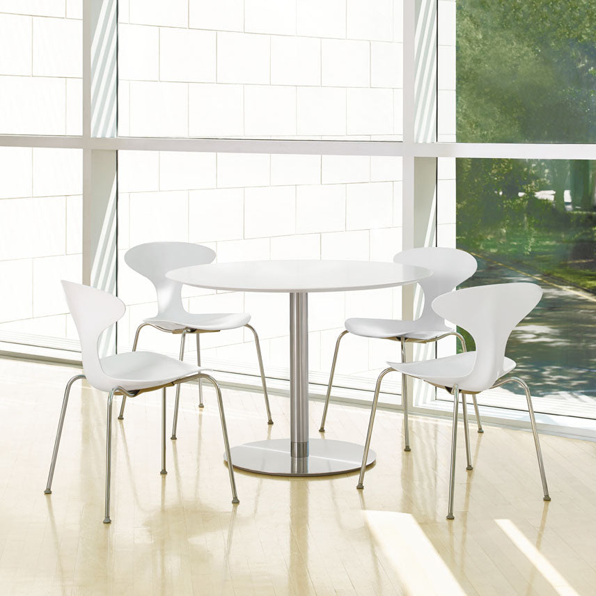 Modern white dining table with chairs in a bright room with large windows.