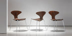Three wooden chairs with metal legs on a white floor and wall