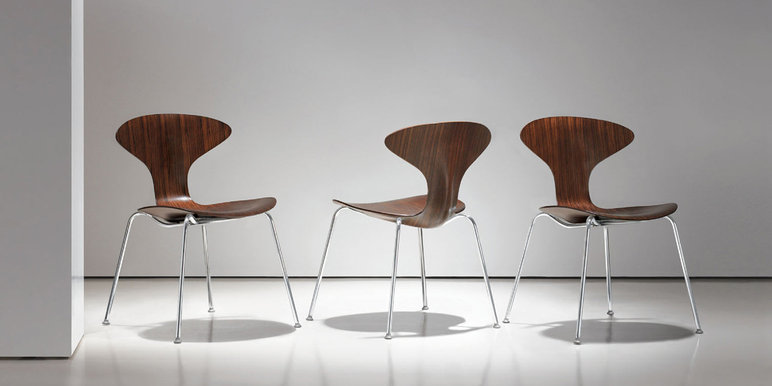 Three wooden chairs with metal legs on a white floor and wall