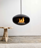 Modern hanging fireplace with flames inside, hanging from the ceiling with a white wall background.